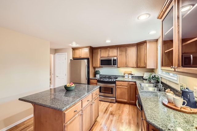 kitchen featuring light wood finished floors, stainless steel appliances, brown cabinetry, a sink, and a kitchen island