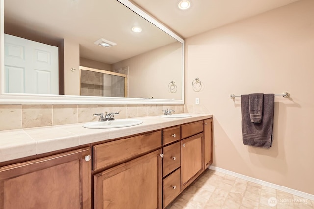 full bathroom with double vanity, a stall shower, baseboards, and a sink