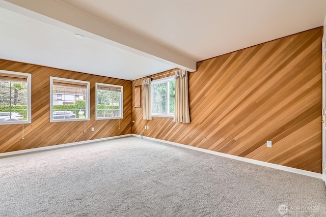 carpeted empty room with wood walls, beam ceiling, and baseboards