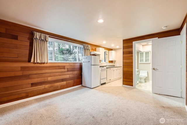 kitchen featuring light colored carpet, wooden walls, a sink, white cabinets, and freestanding refrigerator