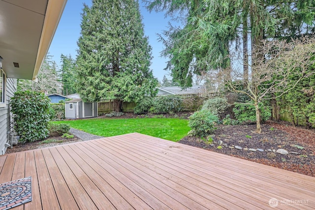 wooden terrace with a storage unit, a lawn, an outdoor structure, and a fenced backyard