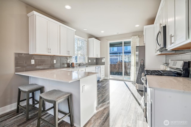 kitchen featuring baseboards, appliances with stainless steel finishes, white cabinets, and wood finished floors