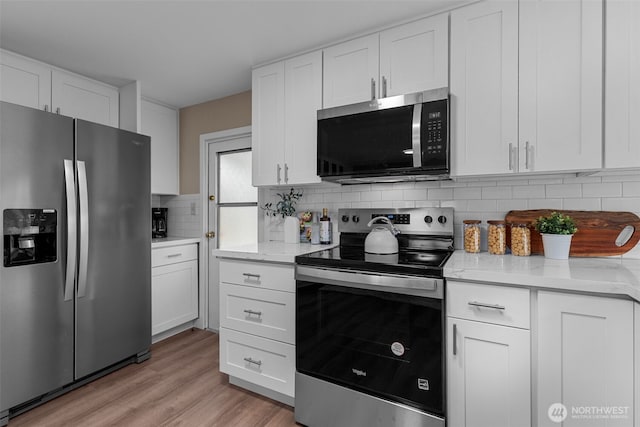 kitchen with light stone countertops, stainless steel appliances, white cabinetry, light wood-style floors, and decorative backsplash
