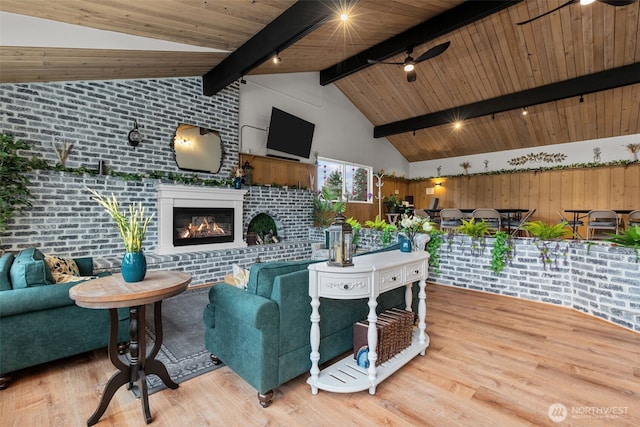 living area with ceiling fan, beam ceiling, wood finished floors, and a glass covered fireplace