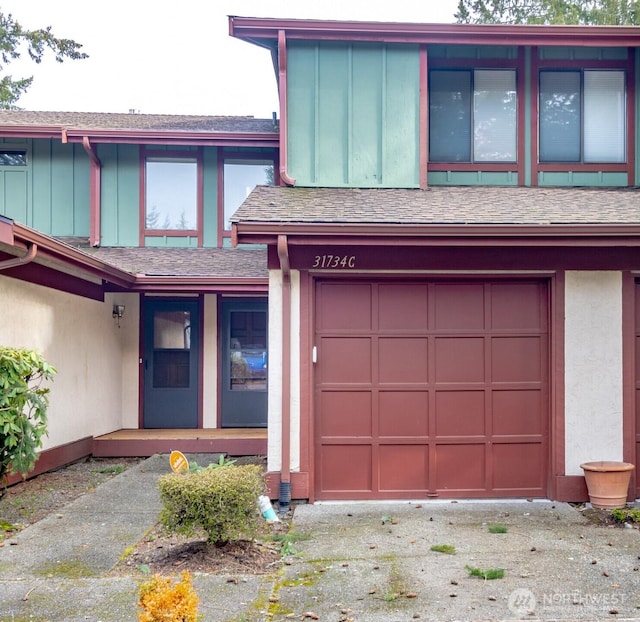 view of front of house with a garage, roof with shingles, board and batten siding, and stucco siding