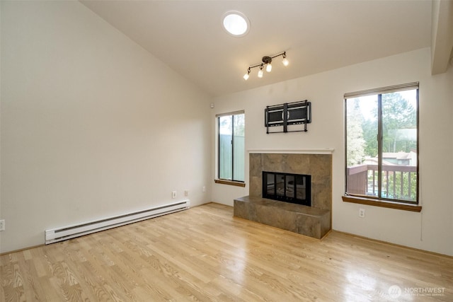 unfurnished living room featuring a baseboard heating unit, a high end fireplace, vaulted ceiling, and light wood finished floors