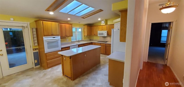 kitchen with white appliances, vaulted ceiling with skylight, brown cabinetry, a center island, and light countertops