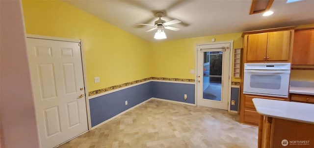 kitchen with light wood-style flooring, ceiling fan, brown cabinets, white oven, and light countertops