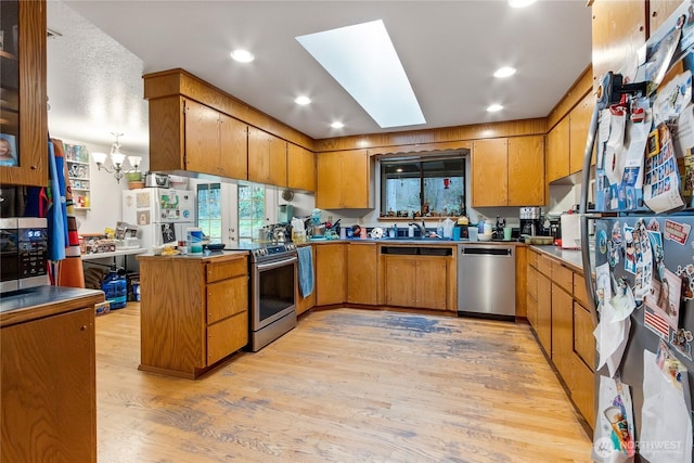 kitchen featuring a peninsula, a skylight, appliances with stainless steel finishes, light wood-type flooring, and brown cabinets