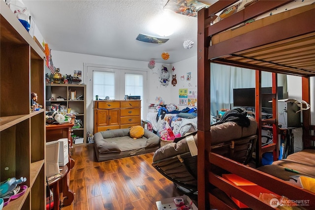 bedroom with a textured ceiling, french doors, and wood finished floors