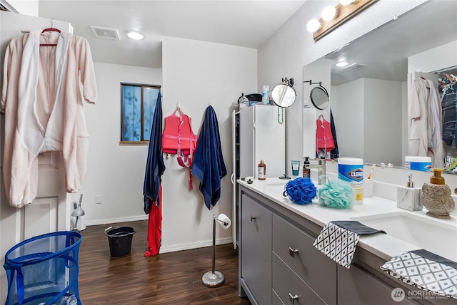 full bath featuring a sink, wood finished floors, visible vents, baseboards, and double vanity