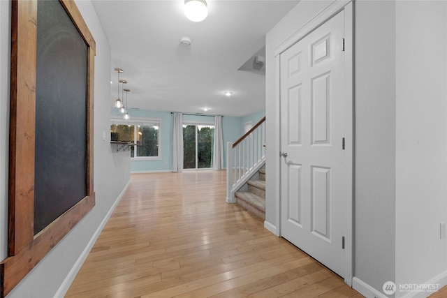 hallway with light wood finished floors, baseboards, and stairway