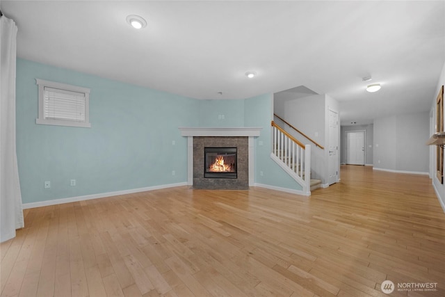 unfurnished living room featuring light wood-style flooring, a fireplace, stairway, and baseboards