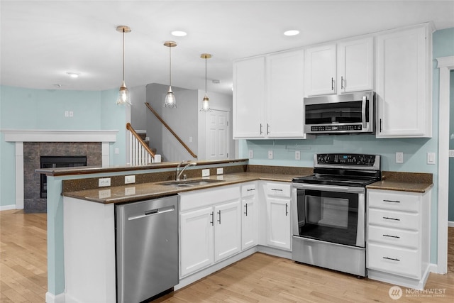 kitchen featuring appliances with stainless steel finishes, a sink, a peninsula, and light wood finished floors