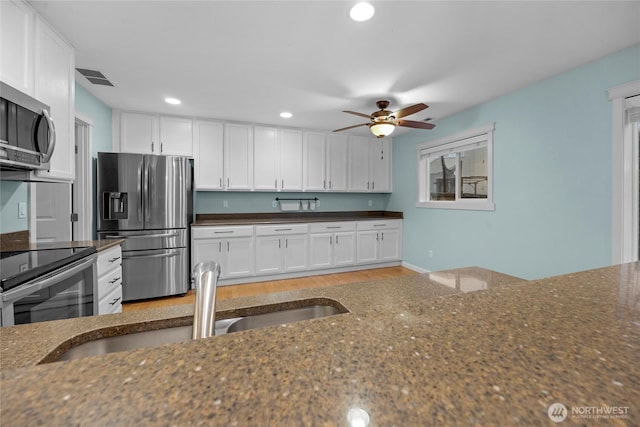 kitchen with white cabinets, appliances with stainless steel finishes, dark stone counters, and a sink