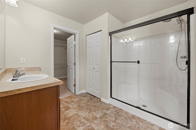 bathroom featuring a shower stall, a spacious closet, baseboards, and vanity