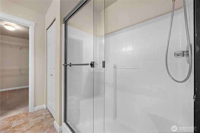 bathroom with a spacious closet, a stall shower, and baseboards