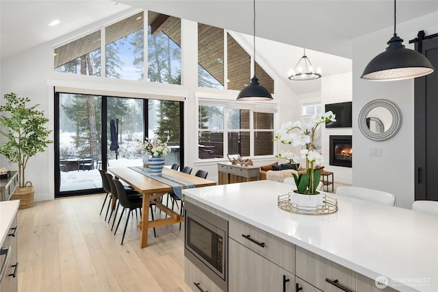 kitchen with a glass covered fireplace, light wood-style flooring, stainless steel microwave, hanging light fixtures, and light countertops