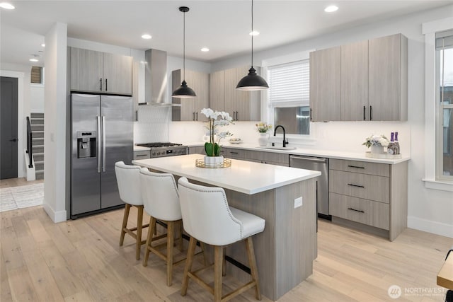 kitchen featuring a breakfast bar area, a sink, appliances with stainless steel finishes, wall chimney exhaust hood, and modern cabinets