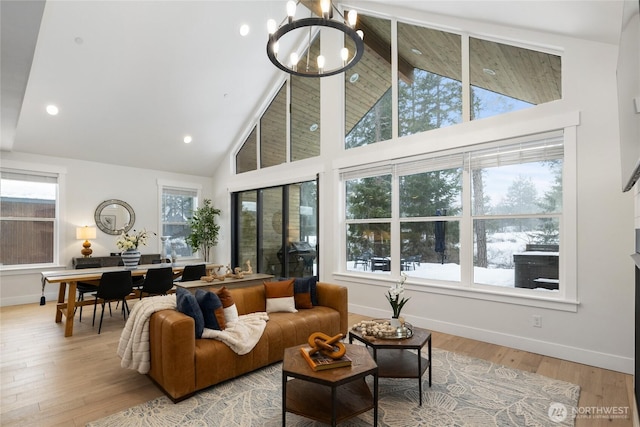 living room featuring high vaulted ceiling, an inviting chandelier, light wood-style flooring, and a healthy amount of sunlight