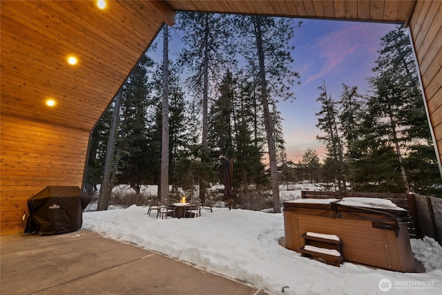 snow covered patio with an outdoor fire pit, grilling area, and a hot tub