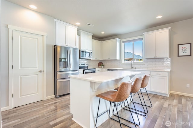 kitchen featuring a center island, stainless steel appliances, light countertops, visible vents, and white cabinets