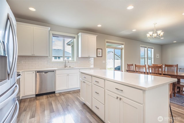 kitchen featuring a sink, light countertops, stainless steel dishwasher, white fridge with ice dispenser, and pendant lighting