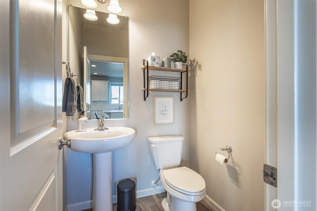 half bathroom featuring wood finished floors, toilet, and baseboards