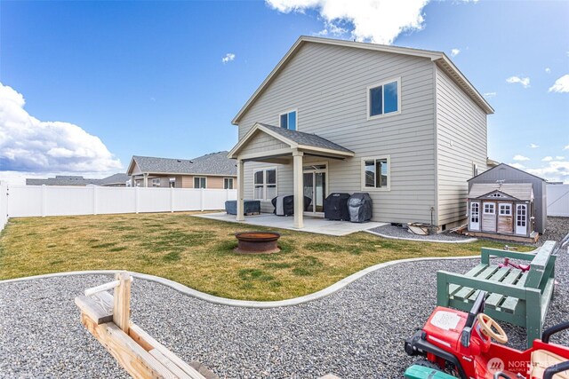 back of house featuring a patio, an outdoor fire pit, a fenced backyard, an outdoor structure, and a yard