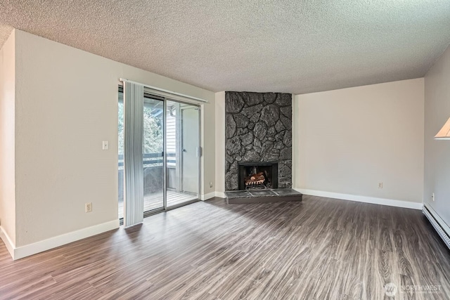 unfurnished living room with baseboards, wood finished floors, a textured ceiling, a stone fireplace, and a baseboard heating unit