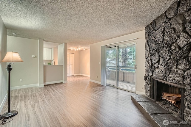 living room with light wood-type flooring, a fireplace, a textured ceiling, and baseboards