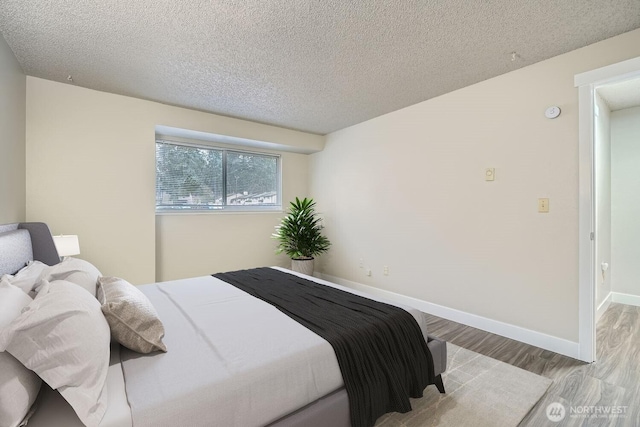 bedroom featuring a textured ceiling, wood finished floors, and baseboards