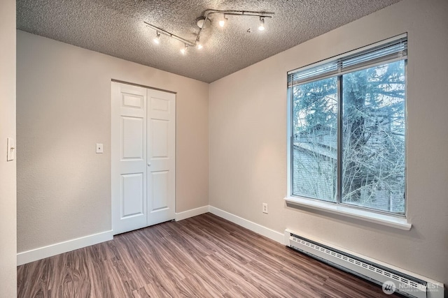 unfurnished bedroom with a textured ceiling, a closet, baseboard heating, and wood finished floors