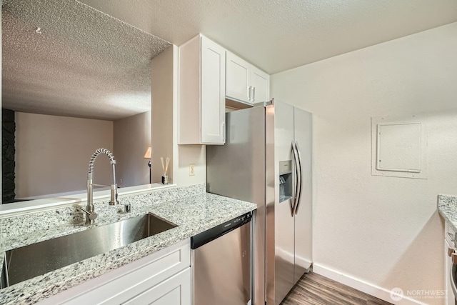 kitchen featuring white cabinets, appliances with stainless steel finishes, wood finished floors, light stone countertops, and a sink