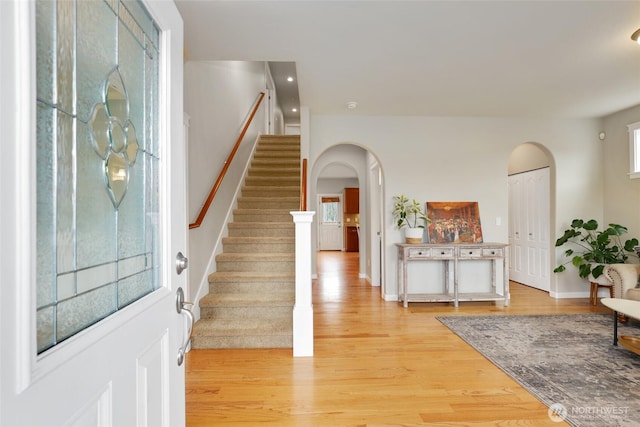 entryway featuring arched walkways, light wood finished floors, stairs, and baseboards