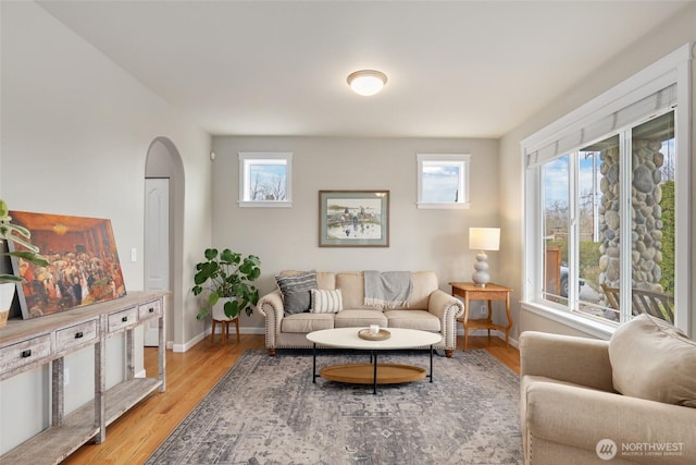 living area featuring a healthy amount of sunlight, baseboards, arched walkways, and wood finished floors