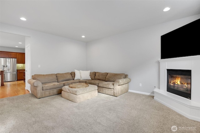 living room featuring recessed lighting, baseboards, light colored carpet, and a glass covered fireplace