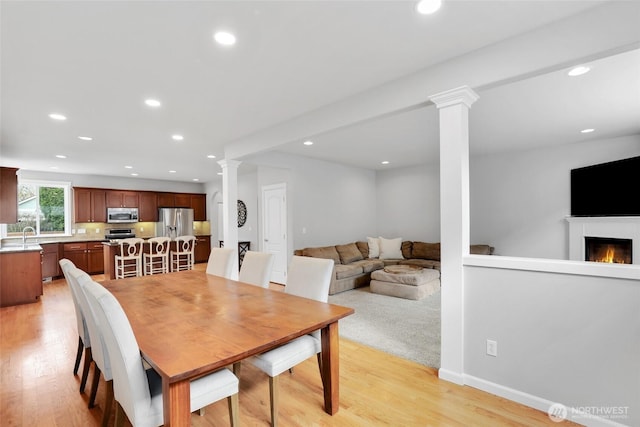 dining area featuring a lit fireplace, light wood-type flooring, decorative columns, and recessed lighting