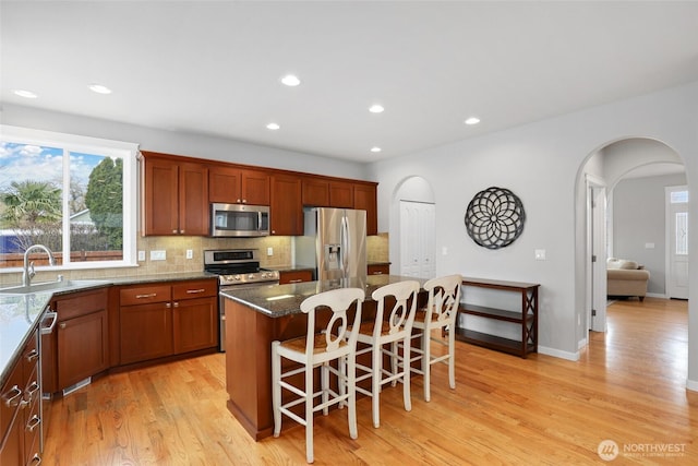 kitchen featuring arched walkways, decorative backsplash, stainless steel appliances, light wood-type flooring, and a sink