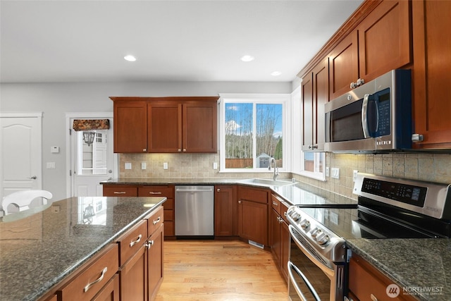 kitchen with stainless steel appliances, a sink, light wood-type flooring, dark stone counters, and tasteful backsplash