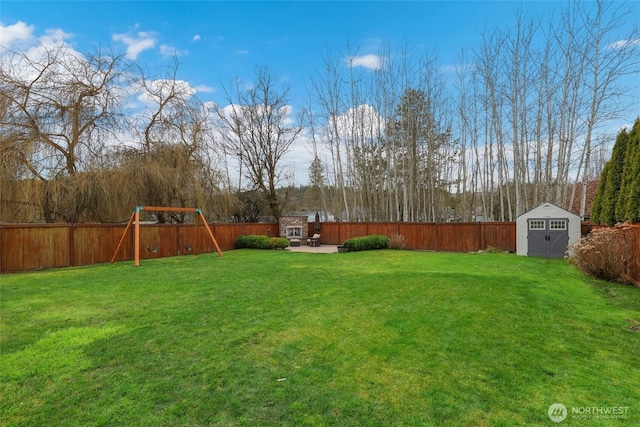 view of yard featuring a storage shed, a playground, a fenced backyard, and an outbuilding