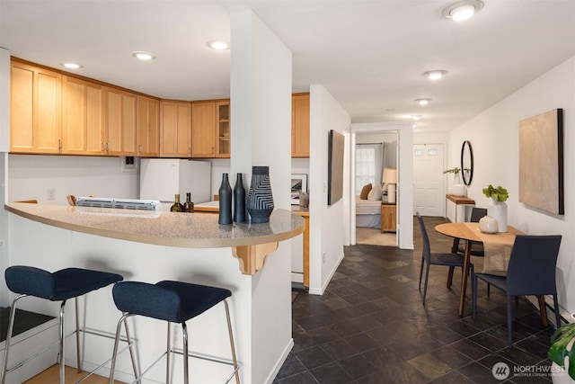 kitchen with a breakfast bar area, a peninsula, light countertops, light brown cabinetry, and glass insert cabinets