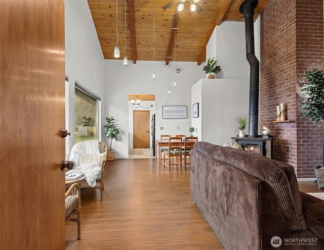 living area featuring a ceiling fan, wood ceiling, a wood stove, wood finished floors, and beamed ceiling