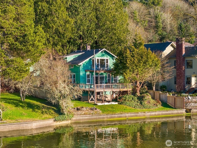 back of property featuring a chimney, fence, a deck with water view, and a yard