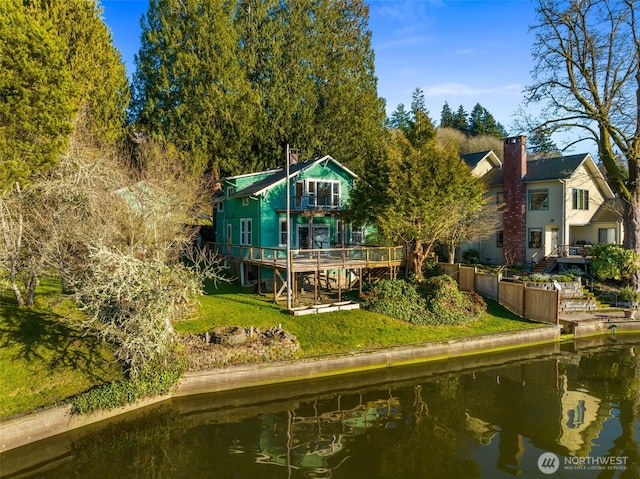 back of property with a lawn, a deck with water view, and a balcony