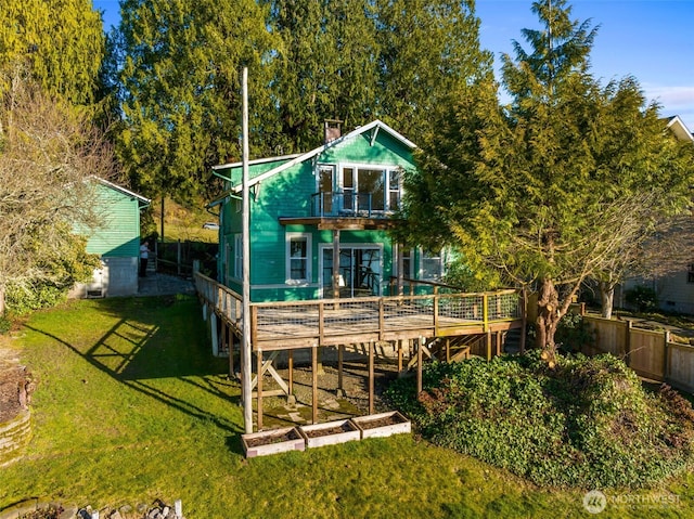 back of property with a balcony, a chimney, fence, and a yard