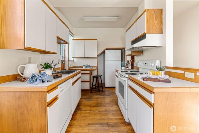 kitchen featuring white cabinets, a sink, wood finished floors, white appliances, and under cabinet range hood