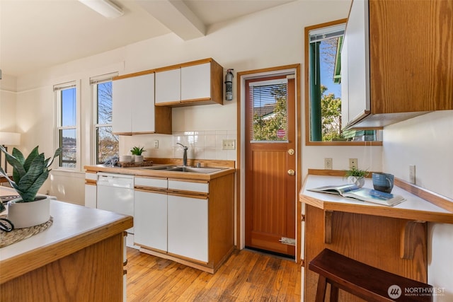 kitchen with a sink, white cabinetry, light countertops, light wood-type flooring, and decorative backsplash