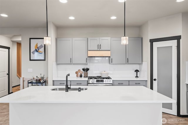 kitchen with a sink, light countertops, gray cabinets, decorative backsplash, and stainless steel range with gas stovetop