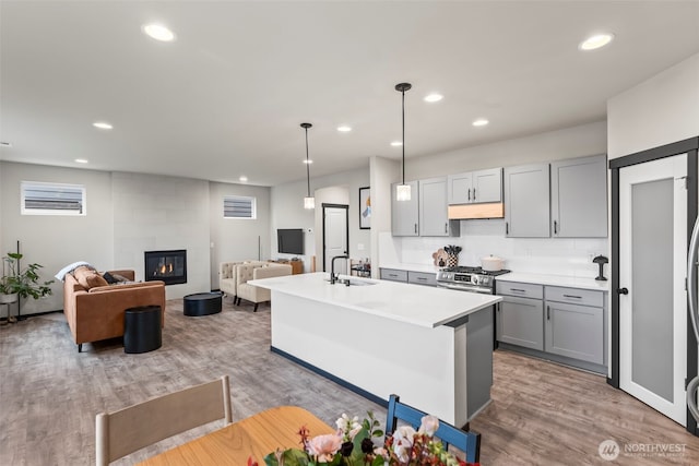 kitchen with gray cabinets, light countertops, a tiled fireplace, stainless steel range with gas stovetop, and wood finished floors